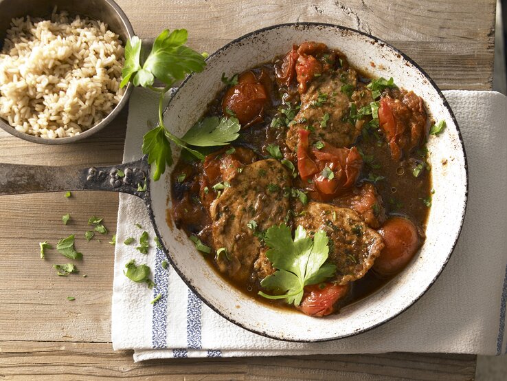Eine Pfanne mit dem Gericht auf einem Holztisch. Daneben noch körniger Reis in einer Schale und alles direkt von oben fotografiert.