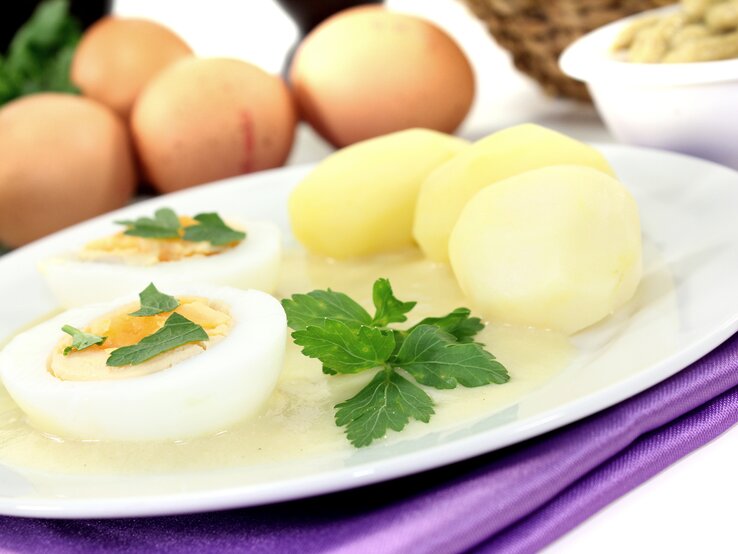 Senfeier auf weißem Teller, daneben Kartoffeln. 