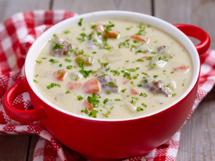 Roter Suppentopf gefüllt mit einer sahnigen Kohlrabisuppe mit Erbsen, Möhren und Hackfleisch. 