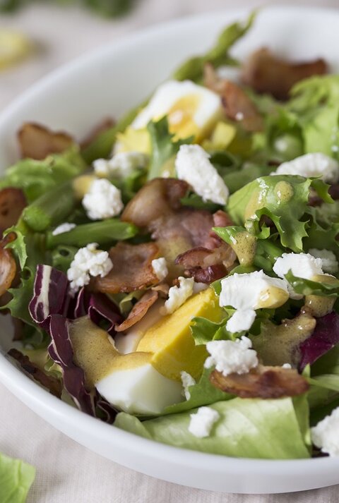 Spargelsalat mit Ei, Speck und Feta auf einem Teller.