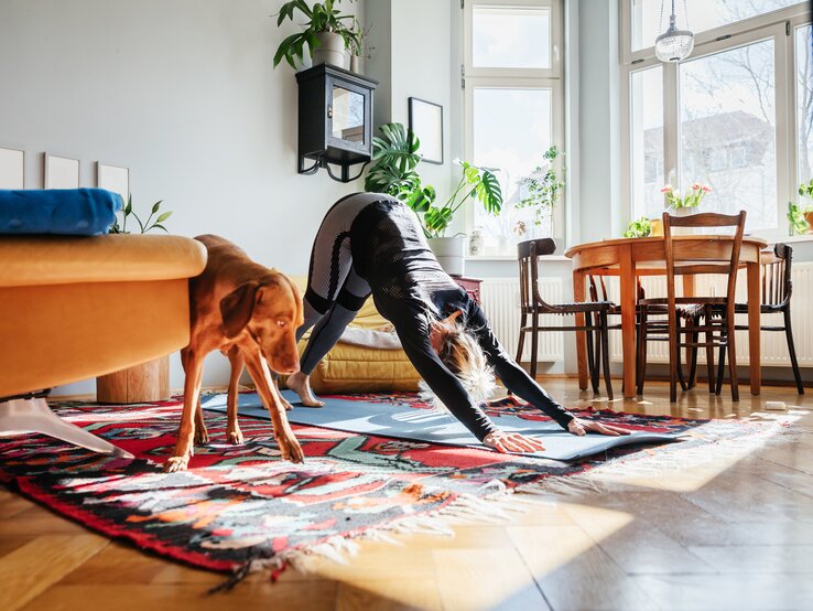 Frau macht Yoga, neben ihr steht ein großer brauner Hund | © Gettyimages/Tom Werner