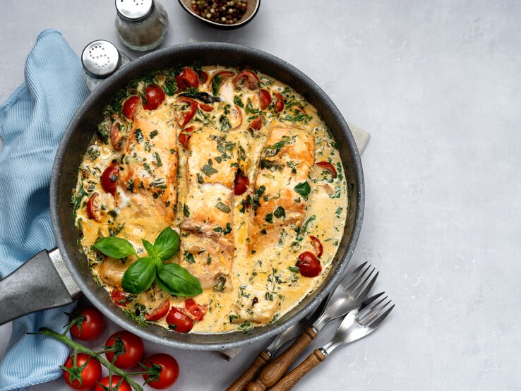 Draufsicht auf eine mediterrane Lachspfanne mit Tomaten & Spinat serviert in einer Pfanne. 