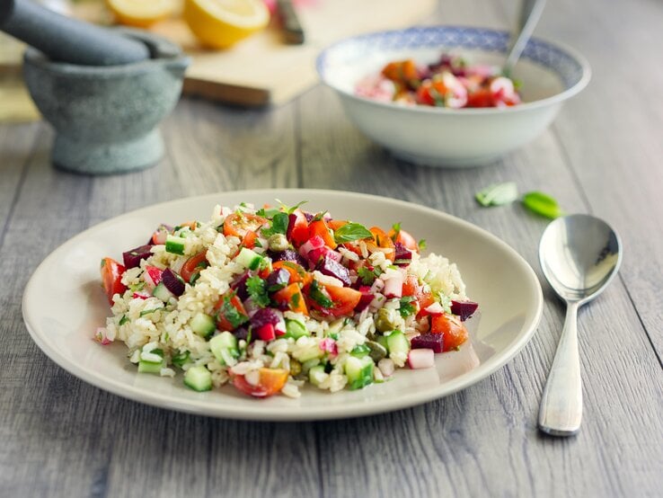 Ein Teller Reissalat mit Curry-Joghurt-Dressing auf einem Untergrund aus Holz / Frontalsicht