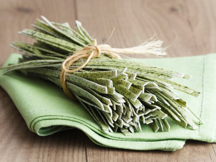 Ein Bündel ungekochte, selbst gemachte Bärlauchnudeln auf einem grünen Tuch, das wiederum auf einem Holztisch liegt. 