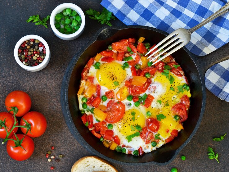 Draufsicht auf eine Eier-Tomaten-Pfanne garniert mit frischen Kräutern.