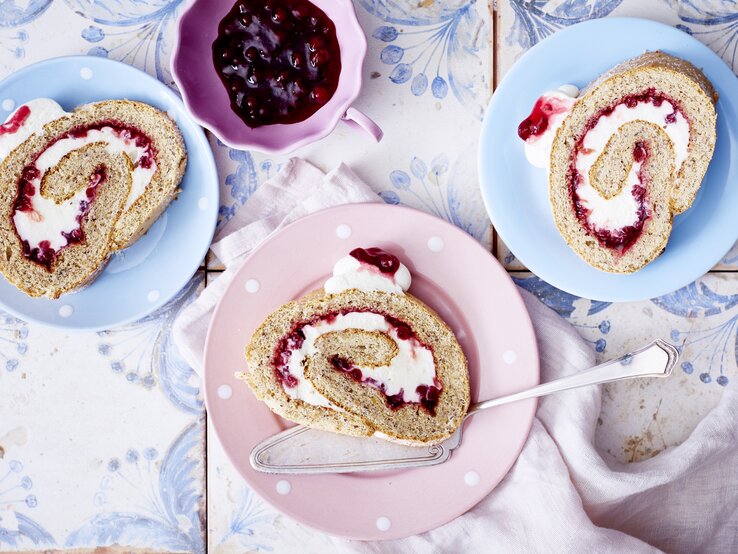 Diese luftig-leichte Kuchenrolle darf auf deinem Kaffeetisch nicht fehlen! Preiselbeer-Nuss-Rolle auf Tellern serviert