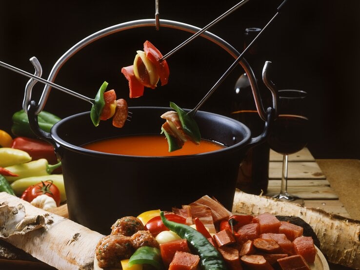 Eine Nahaufnahme eines Topfes mit Tomaten-Fondue, umgeben von Zutaten und einem Glas Rotwein. 