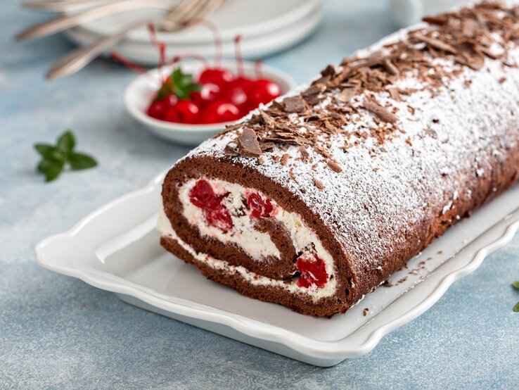 Draufsicht, schräg: Einen perfekten Biskuit, als cremige Rolle mit Sahne, Schokolade und Kirschen.