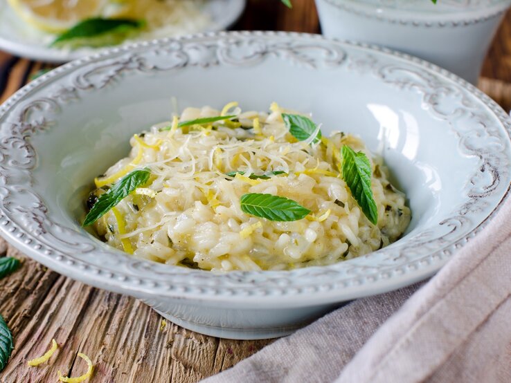 Ein tiefer Pasta-Teller mit Risotto mit Zitrone und Minze auf einem Holztisch.