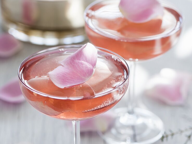 Zwei Champagnergläser mit rosa Sektgelee, in denen essbare Rosenblätter eingeschlossen sind.