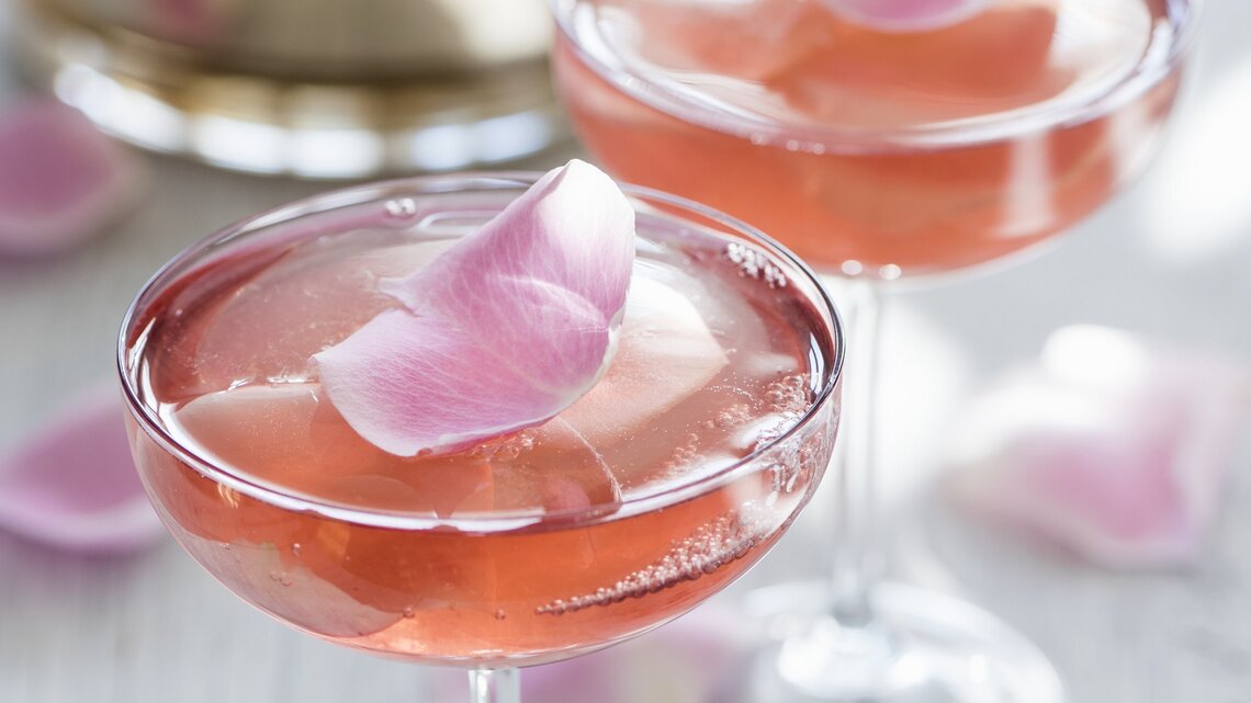 Zwei Champagnergläser mit rosa Sektgelee, in denen essbare Rosenblätter eingeschlossen sind.