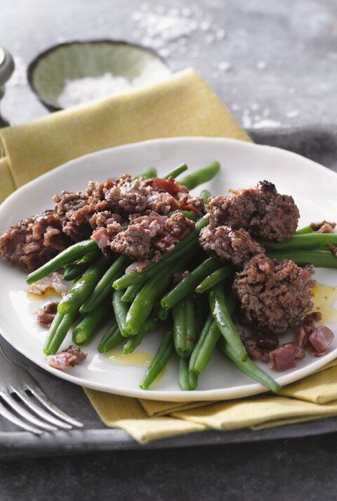 Ein weißer Teller mit der Hackfleischpfanne und en grünen Bohnen auf einem grauen Steintisch. Alles von schräg oben fotografiert.