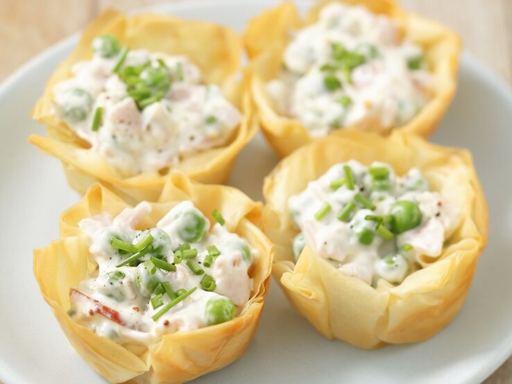 Vier Filoteig mit Schinken, Erbsen und Mayonnaise gefüllt und mit Schnittlauch bestreut / Draufsicht, schräg