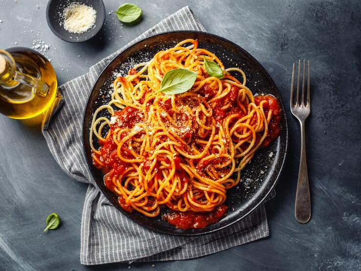 Eine PortiVegane Spaghetti Bolognese / frische Basilikumblätter / runder Teller / Gabel / geriebener Parmesan  / Kleine Flasche mit Öl / Küchentuch /