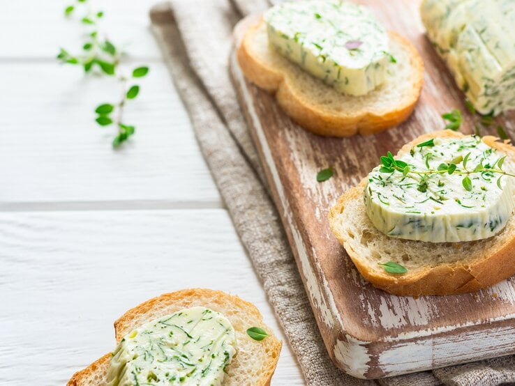 Ein paar Baguette-Scheiben mit Limetten-Koriander-Butter und Kräutern verziert auf einem Brett.