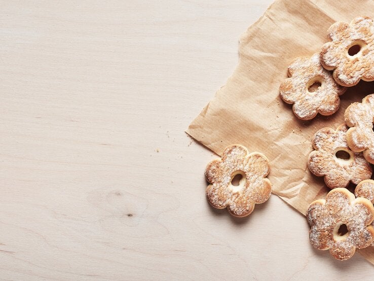 Draufsicht: Auf einem hellen Untergrung liegt braunes Packpapier. Auf dem liegen hellbraune Canestrelli-Kekse in Blumenform.