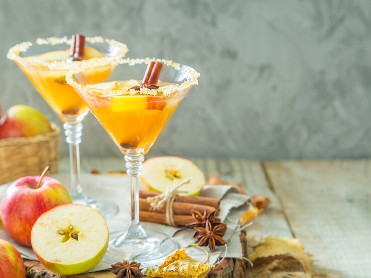 Apfelwein-Mimosa Zwei Martini-Gläser mit dem Getränk auf einem hellen Holztisch von vorne fotografiert.
