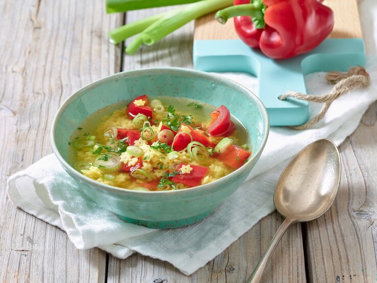 Eine dampfende Schüssel klare Nudelsuppe mit roten Paprikawürfeln, grünen Lauchzwiebelringen und Sternchennudeln.