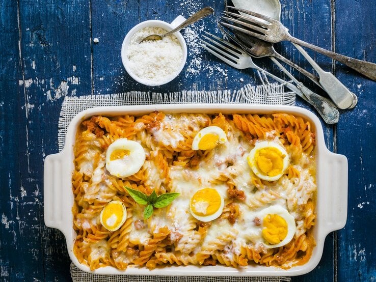 Weiße Form mit Nudelauflauf mit Eiern, daneben Besteck und Parmesan 