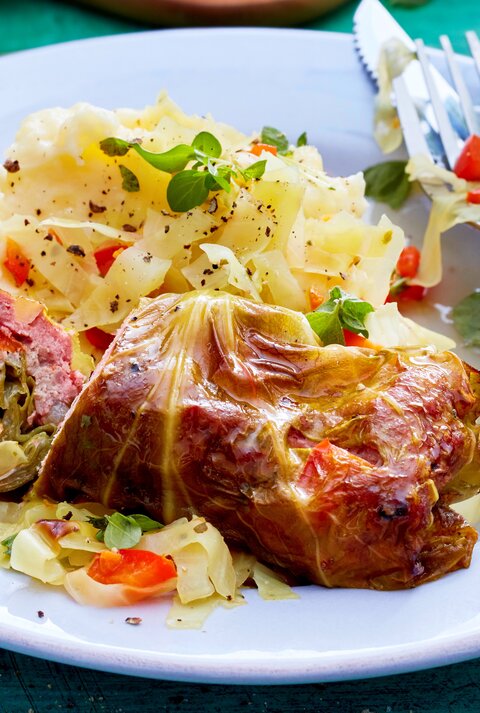 Spitzkohl-Rouladen an Kartoffelpüree auf einem weißen Teller und blauem Untergrund. Alles von schräg oben fotografiert.