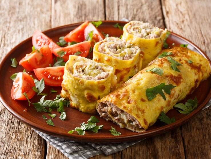 Gefüllte Eierrollen mit Hackfleisch auf einem braunen teller, der auf einem Holztisch steht. 