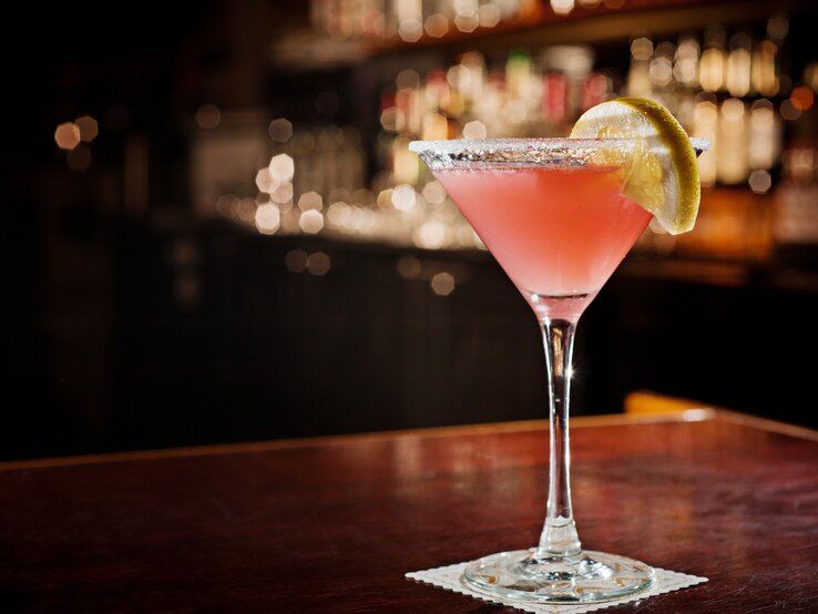 Cosmopolitan Ein liebevoll dekoriertes Glas mit Cosmoolitan in einer dunkleren Bar-Atmosphäre.