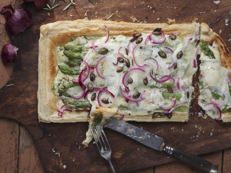Ein dunkles Holzbrett mit der Tarte auf einem Holztisch direkt von oben fotografiert.