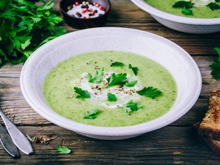 Zucchinicremesuppe Eine helle, runde Schale gefüllt mit einer cremigen, sahnigen Zucchinisuppe.