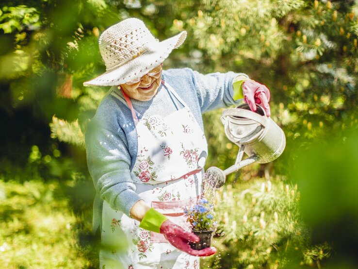 Eine ältere Frau gießt in ihrem Garten ein Blumentöpfchen in ihrer Hand | © Getty Images/ Eva-Katalin