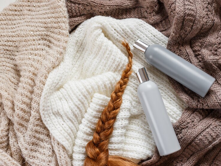 Gestrickte Kleidung, ein geflochtener Zopf aus rotem Haar und Conditioner – als Wollpflegemittel. | © iStock/Vladdeep