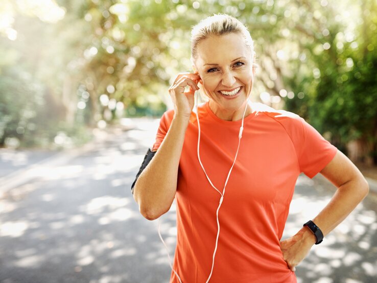 Frau in der Natur beim Joggen, sie richtet ihre Ohrhörer | © iStock/PeopleImages