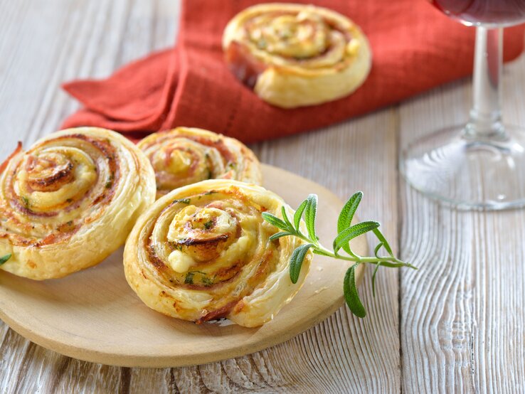 Blätterteigschnecken mit Schinken und Käse  auf hellem Holz. 