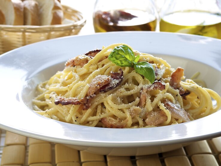 Weißer Pasta-Teller befüllt mit original Spaghetti Carbonara mit italienischem Speck und geriebenem Hartkäse.