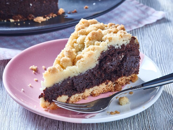 Ein angeschnittenes Stück Schokoladenkuchen mit hellem Streusel-Topping auf einem Teller.
