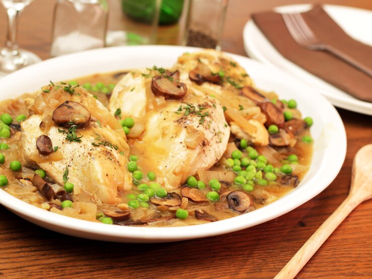 Ein weißer Teller mit dem Hühnerfrikassee auf einem rustikalen Holztisch. Alles von schräg oben fotografiert.