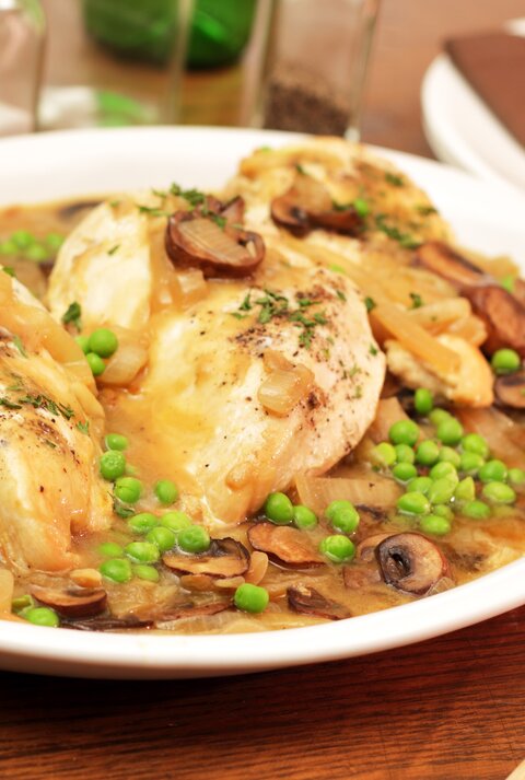 Ein weißer Teller mit dem Hühnerfrikassee auf einem rustikalen Holztisch. Alles von schräg oben fotografiert.