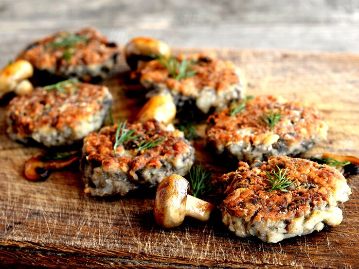 Frikadellen gehen sogar vegetarisch! Dafür am besten die Pilz-Saison nutzen und die Leckerbissen aus Champignons herstellen. Mehrere vegetarische Pilzfrikadellen auf einem Holzbrett.