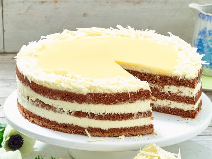 Die weiße Schokoladentorte auf einem Tortenständer und Holztisch. Alles von der Seite fotografiert.