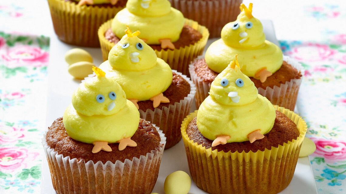 Gelbe Küken-Cupcakes mit blauen Augen und orangen Füßen auf einer Etagere.
