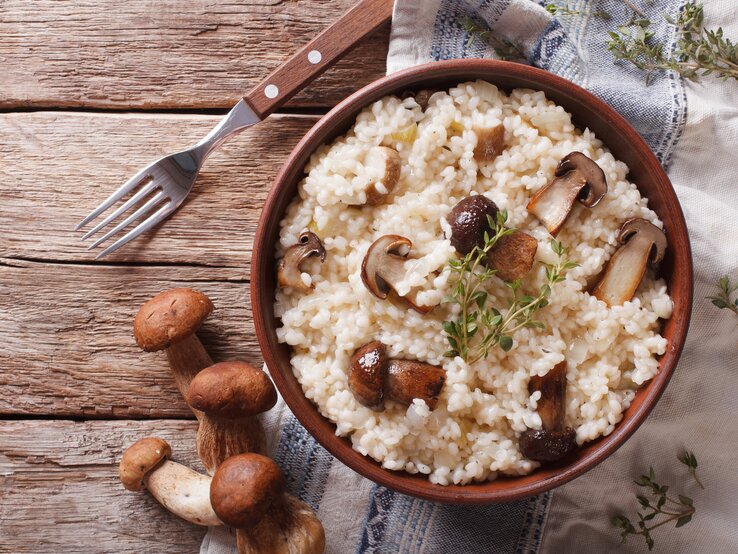Draufsicht auf einen Teller mit Steinpilz-Risotto auf einem Holztisch.