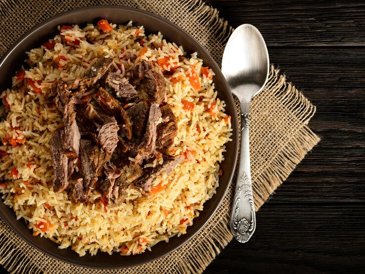 Draufsicht auf eine Reispfanne mit gebratenem Rindfleisch auf braunem Teller. 