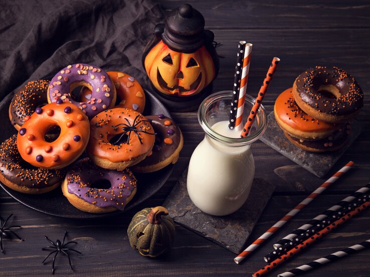 Eine tolle Idee für das Halloween-Dessert – selbst gemachte Halloween-Donuts, die mit Kürbismus gefüllt sind und gebührend dekoriert sind.  verschieden dekortierte Halloween-Donuts auf einem Teller.