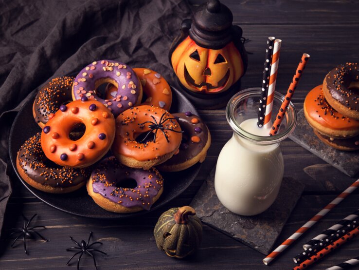 Eine tolle Idee für das Halloween-Dessert – selbst gemachte Halloween-Donuts, die mit Kürbismus gefüllt sind und gebührend dekoriert sind.  verschieden dekortierte Halloween-Donuts auf einem Teller.