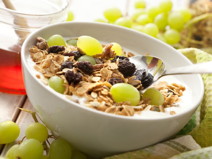 Trauben-Muesli Eine weiße Schale mit dem Traubenmüsli und frischen Weintrauben auf einem dunklen Holztisch. Alles nah und von der Seite fotografiert.