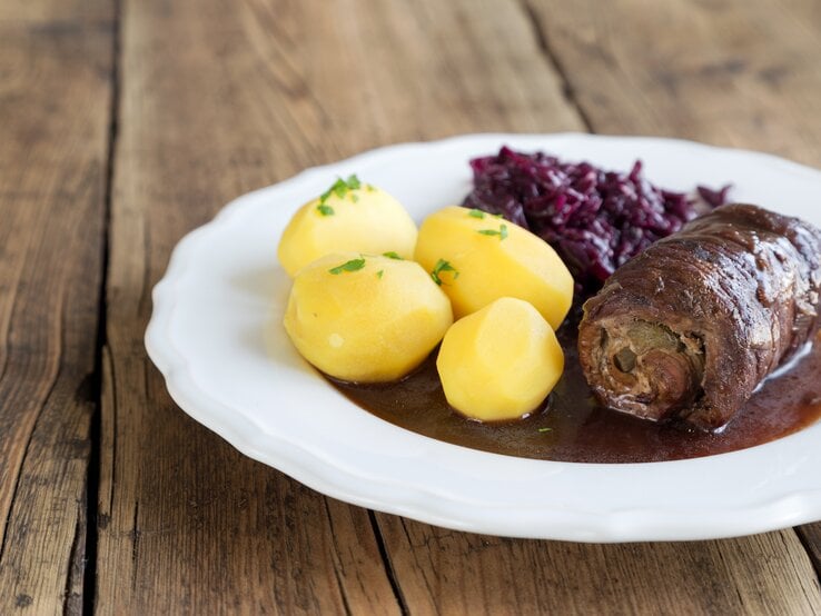 Ein weißer Telle rmit den Roualdne udn Beilagen auf einem rustikalen Holztisch. Alles nah und von der Seite fotografiert.