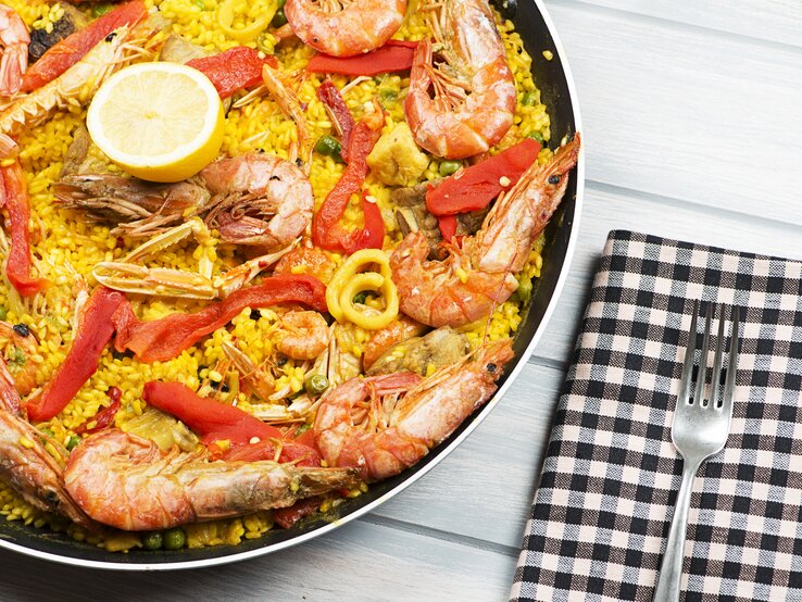 Eine schwarze Pfanne mit dem gelben Reis und Meeresfrüchten auf einem weißen Holztisch.