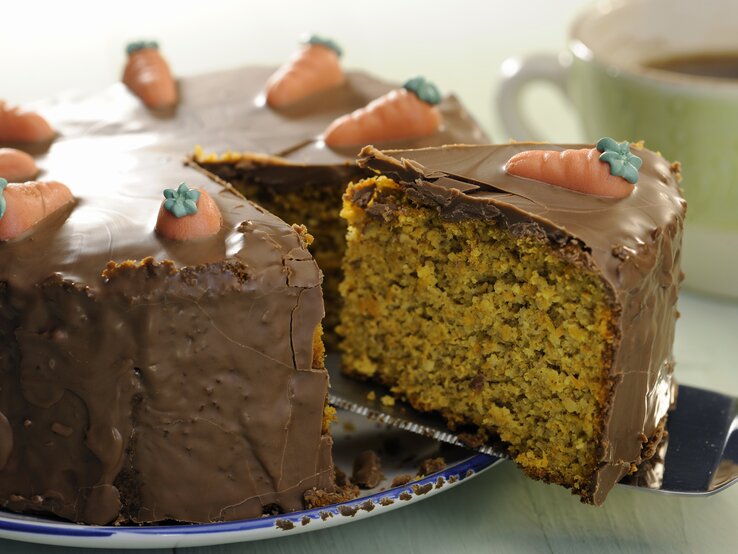 Eine Nahaufnahmen vom Schoko-Möhrenkuchen und gerade wird ein angeschnittenes Stück rausgenommen mit dem Tortenheber.