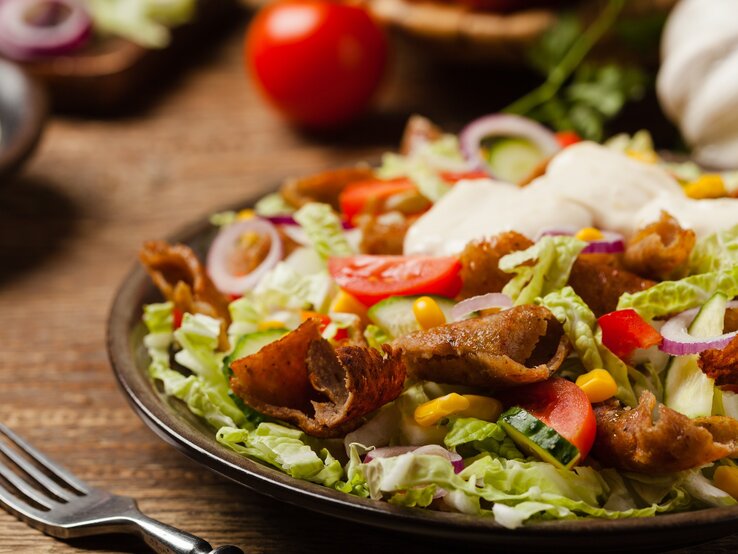 Ein schwarzer Teller auf einem Holztisch mit dem Gyros-Salat von der Seite fotografiert.