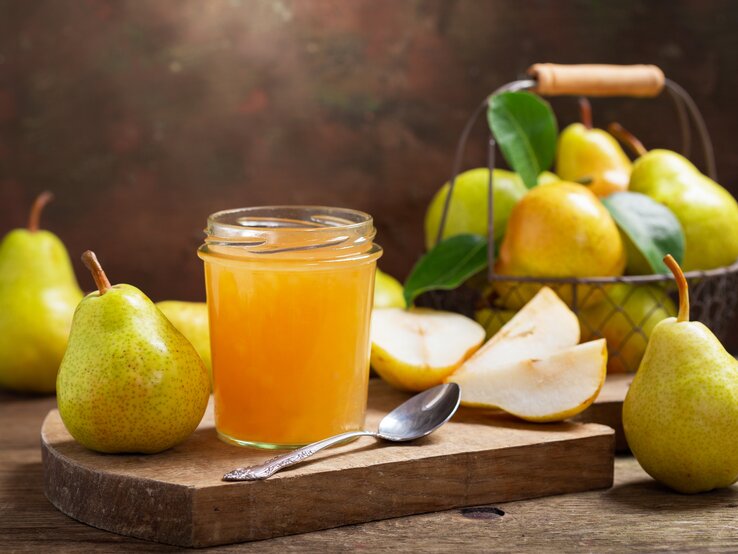 Birnenmarmelade Ein Glas mit Birnenmarmelade auf Holzbrett in rustikalem Ambiente. Daneben viele frische Birnen.