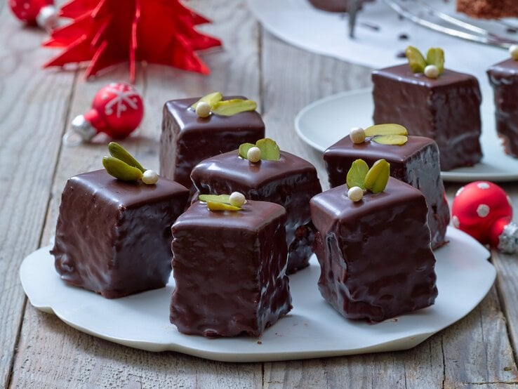 Pistazien-Dominosteine auf zwei runden Tellern / kleine Weihnachtskugeln / Untergrund Holz / Frontalsicht
